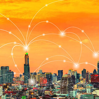 Wireless network connection technology icons over city at sunset.